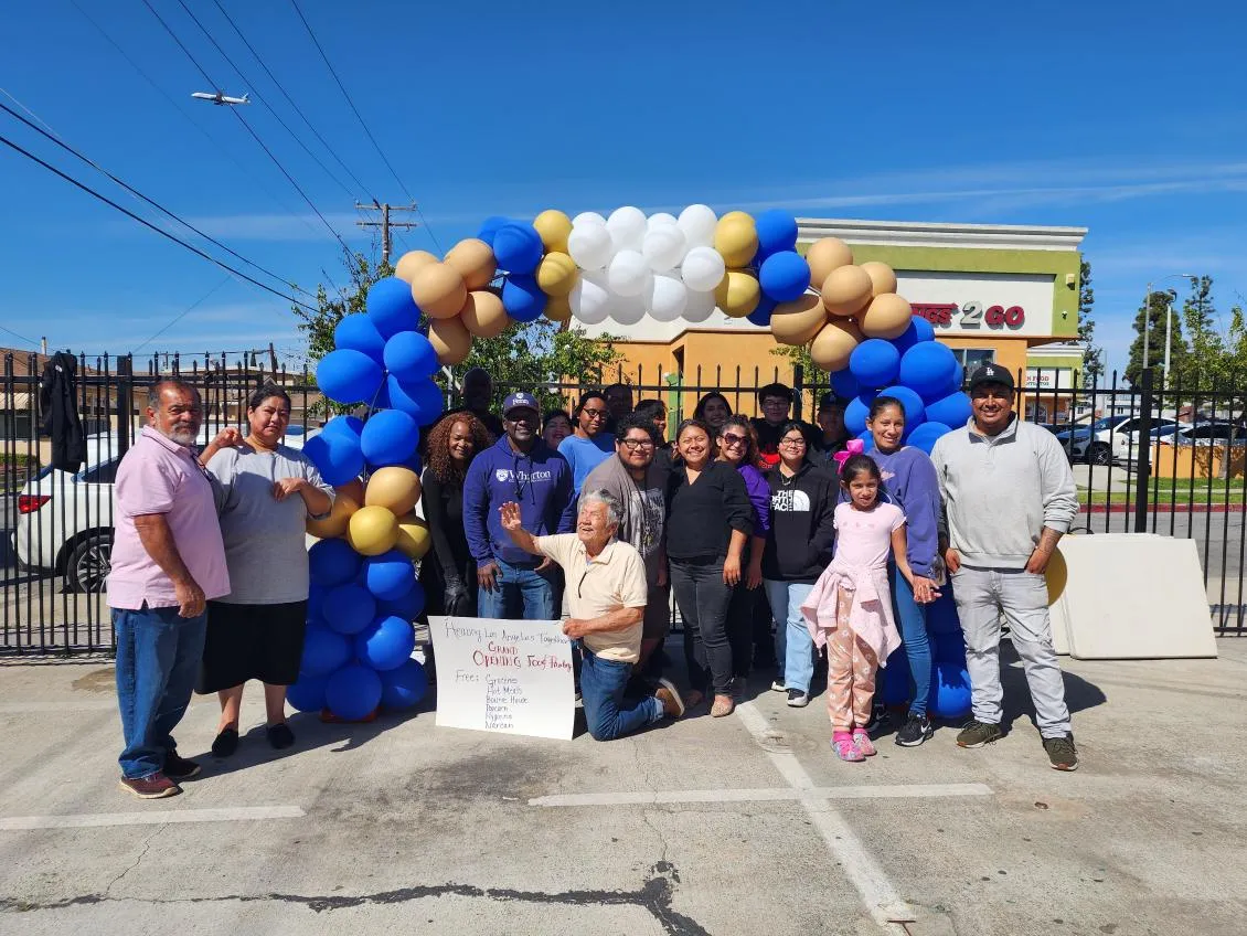 HLAT team and neighbors under a blue and gold balloon arch at the Eat Manna food pantry grand opening