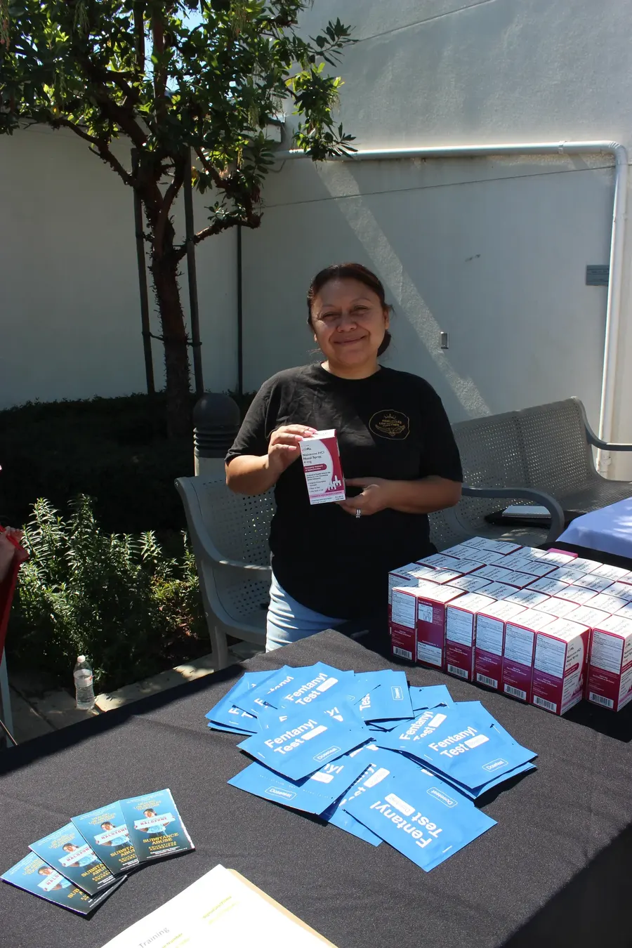 HLAT team member holding Narcan at an outreach table with fentanyl test strip packets